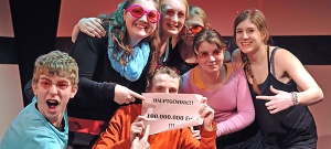 Jugendliche stehen im Pulk zusammen. Sie tragen rosa Sonnenbrillen und halten ein Schild hoch. Auf dem Schild steht: "Hauptgewinn!!! 100.000.000 Euro!!!"