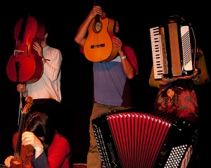 Drei Personen halten sich Musikinstrumente vor das Gesicht.