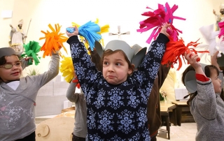 Kinder tanzen mit bunten Pompoms. Sie tragen selbstgebastelte Mäuseohren auf dem Kopf.