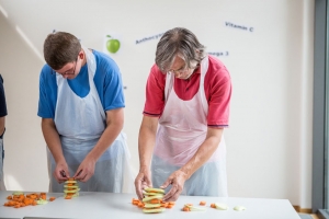 Zwei Männer stapeln Kohlrabi und Möhrenscheiben aufeinander.