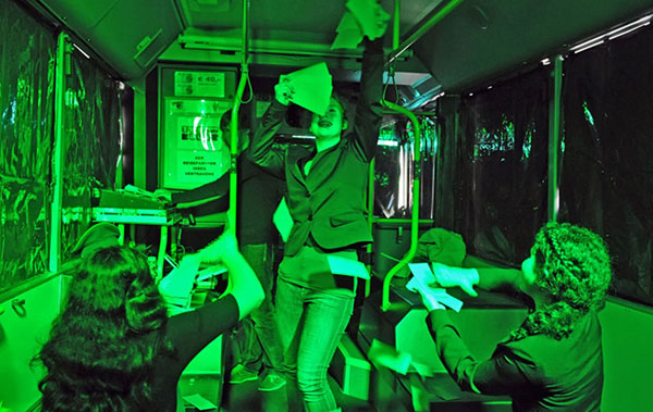 Eine Frau tanzt durch einen Bus. Sie hält mehrere Scheine in der Hand. Weitere Passagiere jubeln ihr zu. Der Bus ist grün beleuchtet, die Scheiben sind mit Folie verklebt.