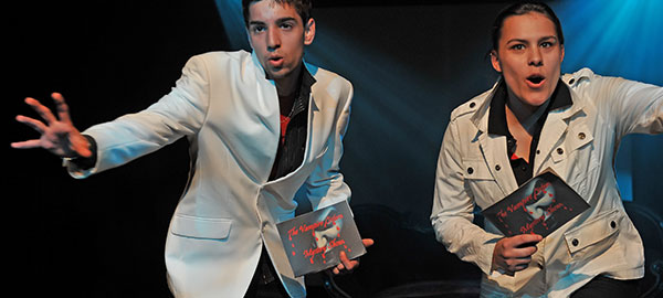 Zwei Personen in weißen Anzügen präsentieren ein Buch in ihren Händen. Auf dem Buch ist das Gesicht eines Vampirs abgebildet.