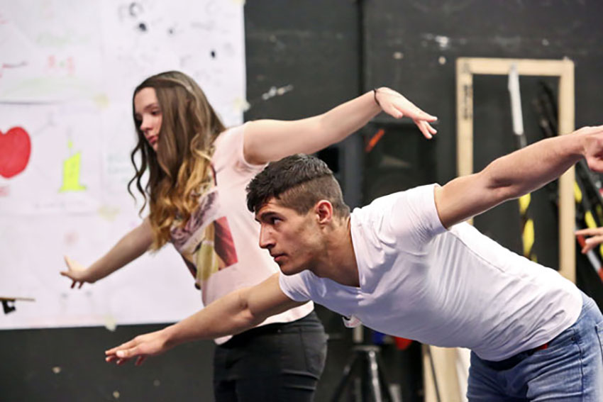 Ein junger Mann und eine junge Frau tanzen gemeinsam auf der Bühne. Sie breiten die Arme aus, als wollten sie fliegen.