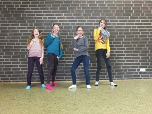 Vier Mädchen stehen vor einer Mauer und posieren lachend.