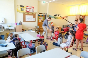 Kinder und zwei Theaterpädagog*innen stehen in einem Klassenzimmer und drehen gemeinsam einen Film.