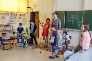 Zwei Theaterpädagog*innen und Kinder einer Grundschulklasse stehen mit Film-Equipment vor einer Tafel.