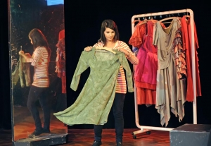 Eine Frau hängt ein grünes Kleid auf einen Kleiderbügel. Im Hintergrund hängen weitere Kostüme an einem Kleiderständer.