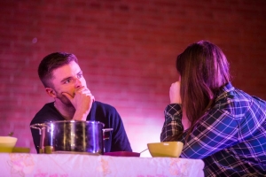 Ein Mann und eine Frau sitzen zusammen am Esstisch und unterhalten sich. Der Mann sieht erschrocken aus.