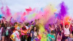 Viele junge Leute werfen bunte Farben in die Luft. Die Leute lachen.