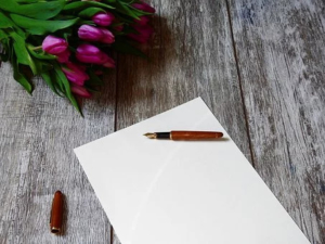 Ein Blatt Papier liegt auf einem Holztisch. Auf dem Blatt Papier liegt ein Füller. Über dem Füller liegt ein Strauß Tulpen.