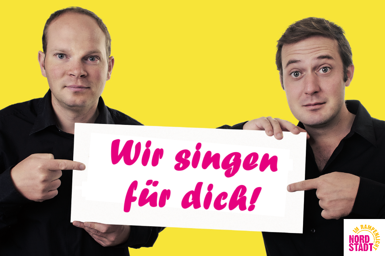 Zwei Männer halten ein Schild in die Kamera. Auf dem Schild steht: "Wir singen für dich!" Der Hintergrund des Bildes ist gelb.