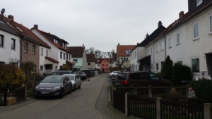 Eine Spielstraße in Hildesheim. Links und rechts sind Wohnhäuser. Rechts parken zwei Autos. Eine Katze läuft über die Straße.