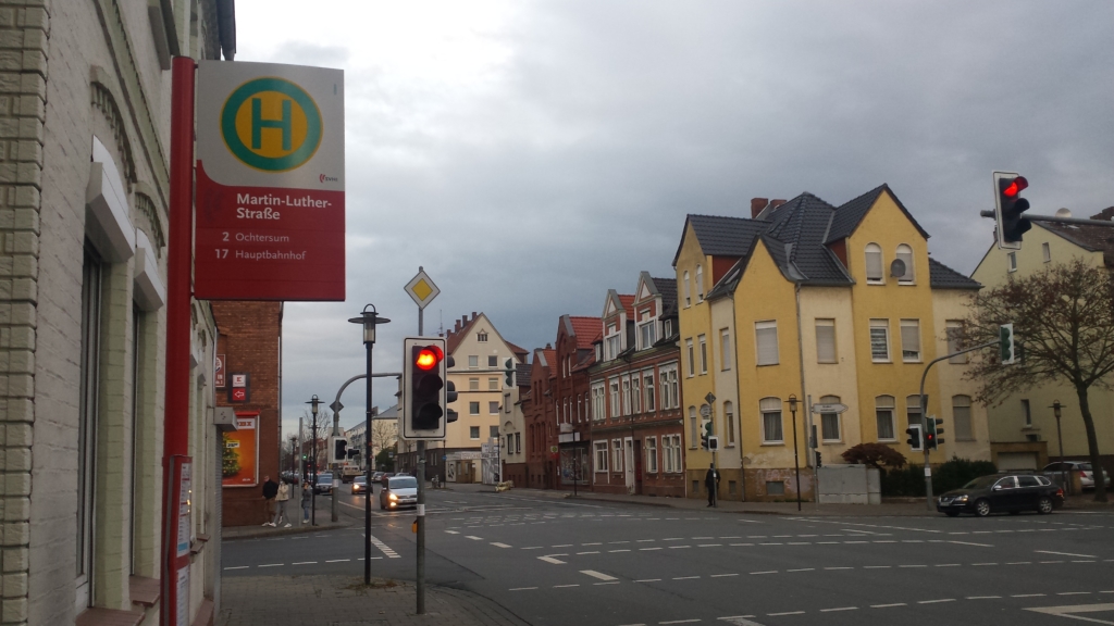 Eine Straße in Hildesheim. Links befindet sich eine Bushaltestelle mit dem Namen "Martin-Luther-Straße". Rechts befindet sich ein gelbes Gebäude und eine Ampel.