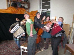 Fünf Personen mit verschiedenen Musikinstrumenten stehen in einem Raum.