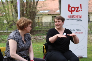 Links im Bild befindet sich die Sozialministerin Daniela Behrens. Sie sitzt auf einem gelben Stuhl auf einer Wiese. Neben ihr sitzt die Geschäftsführerin vom TPZ Katrin Löwensprung. Die beiden Frauen unterhalten sich.
