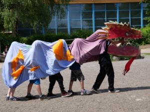 Kinder tragen einen gebastelten Drachen. Der rote Kopf des Drachen besteht aus Pappe, der Körper besteht aus bunten Bettlaken.