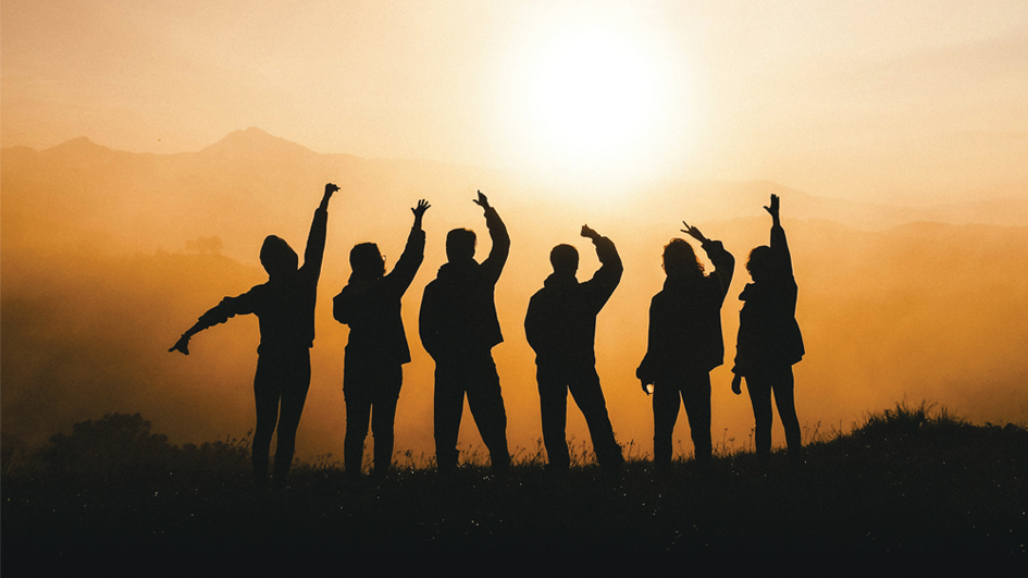 Eine Gruppe von Jugendlichen steht vor einem Sonnenaufgang. Von den Jugendlichen sind nur die Silhouetten zu sehen.