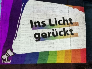 Eine bunte Lichtkunst-Projektion an einer Hausfassade. Dort steht: "Ins Licht gerückt".