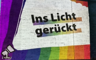 Eine bunte Lichtkunst-Projektion an einer Hausfassade. Dort steht: "Ins Licht gerückt".