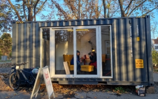 Zwei Personen sitzen in einem Schiffscontainer und unterhalten sich.