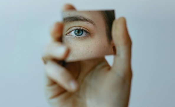 Eine Hand hält eine Spiegelscherbe, in der sich ein Auge spiegelt.