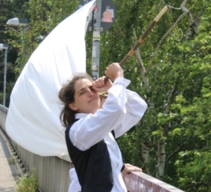 Eine Frau schaut durch ein Fernrohr. Hinter ihr weht eine weiße Flagge.