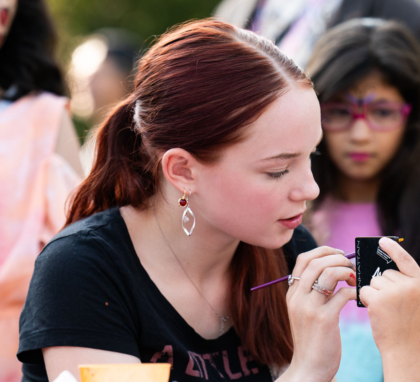 Eine junge Frau trägt Make up auf. Im Hintergrund sieht man ein Kind mit Theaterschminke.