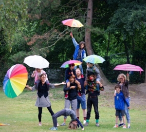 Kinder und Erwachsene turnen gemeinsam auf einer Wiese und halten bunte Regenschirme in den Händen.